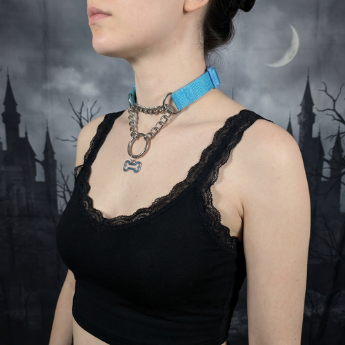 Person wearing a black lace top with a blue collar and chain necklace against a dark, gothic background.