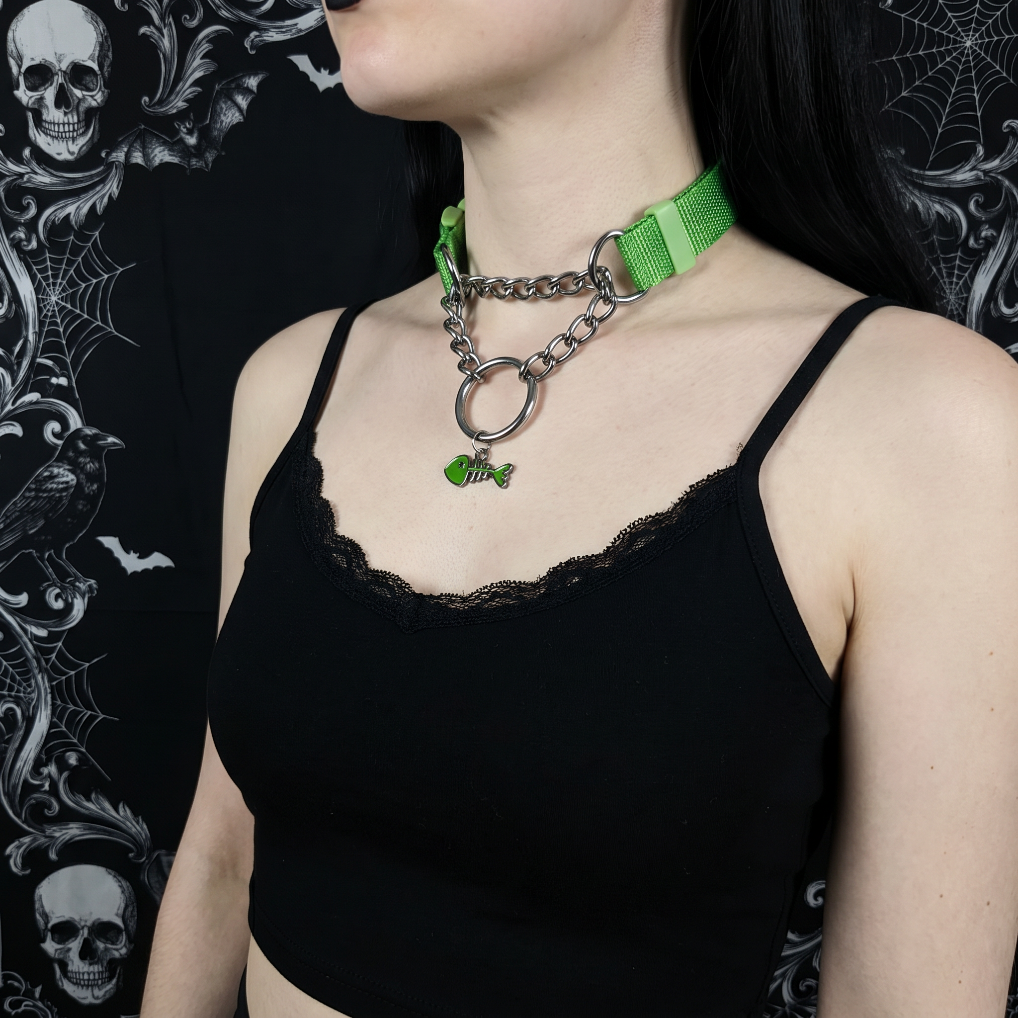 Person wearing a black tank top with a green necklace against a dark, decorative background.