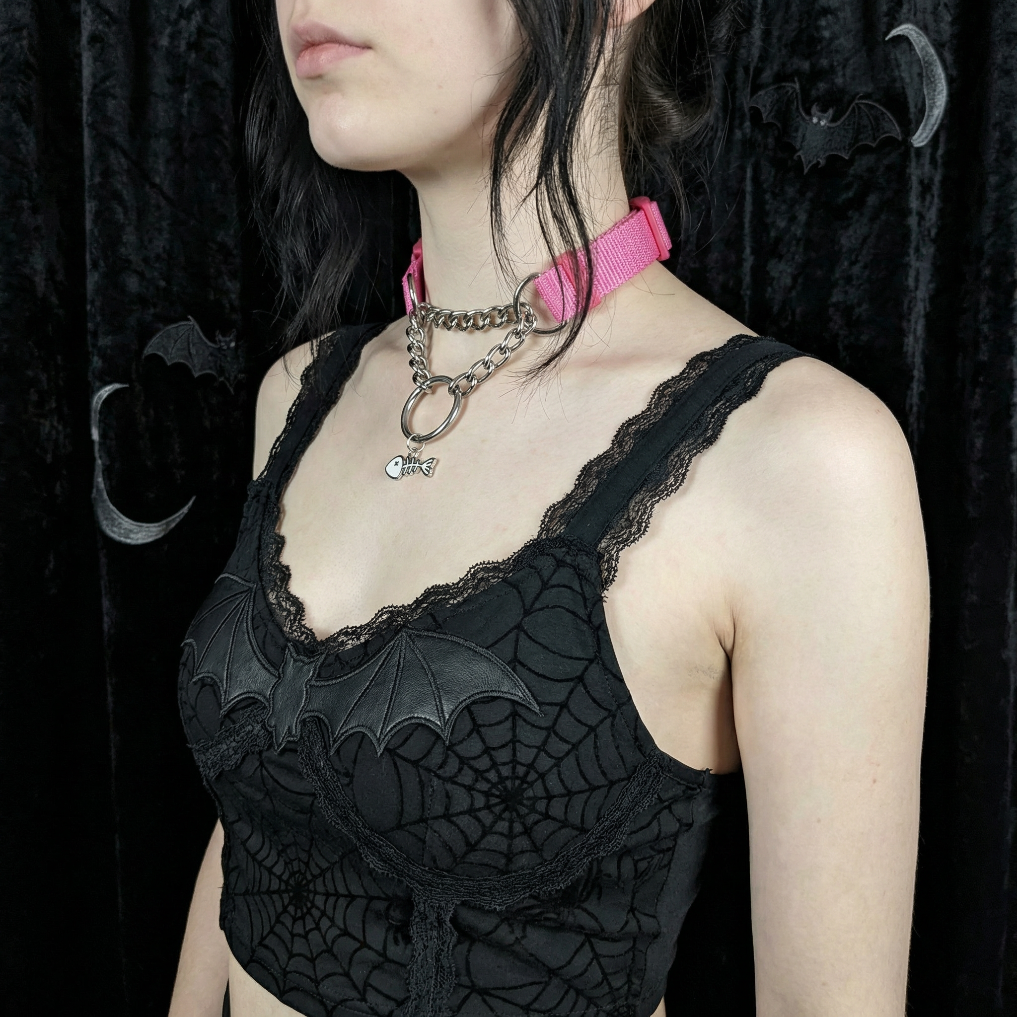Person wearing a black top and pink pull-chain choker necklace against a dark background