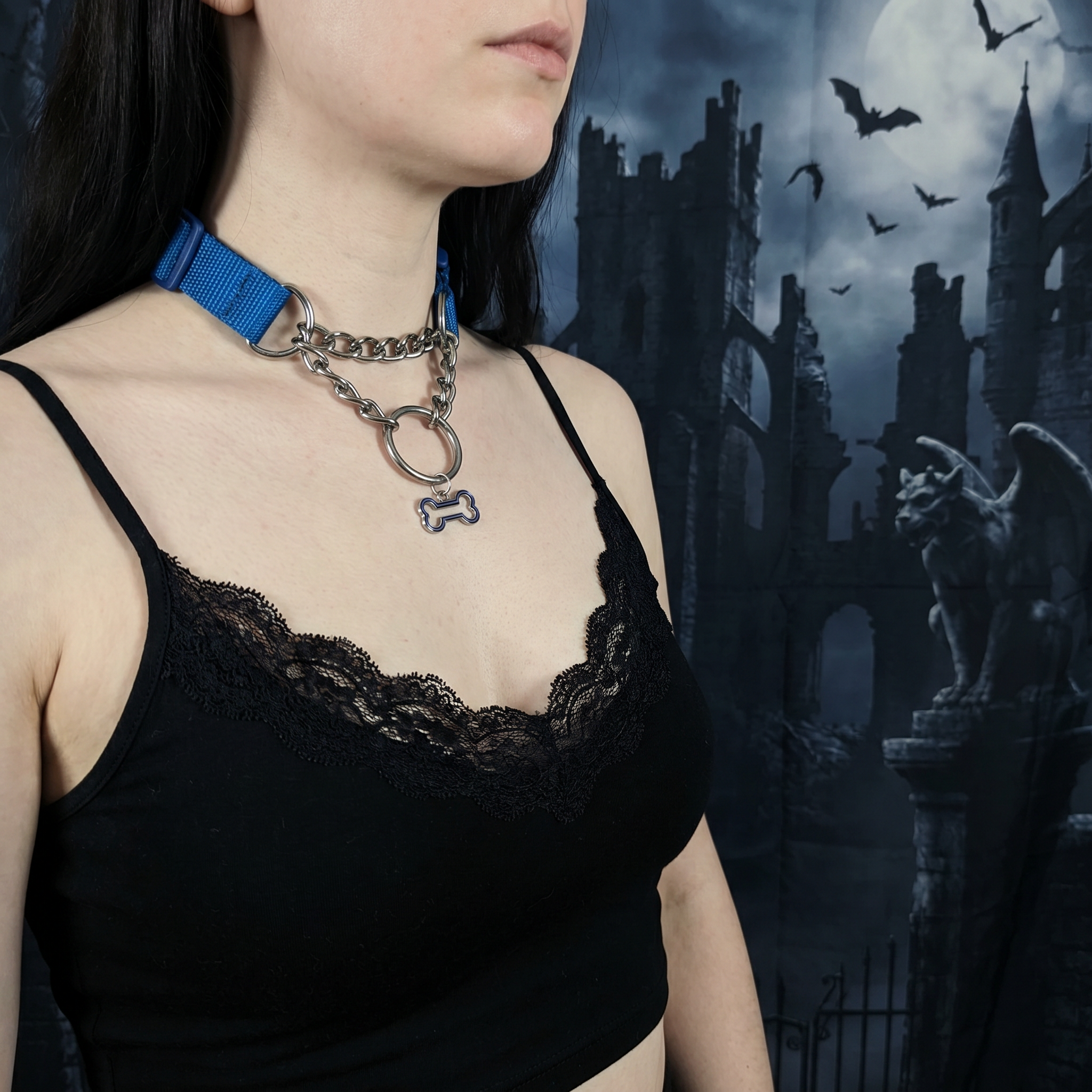 Person wearing a black lace top with a blue collar and chain necklace against a gothic castle background.