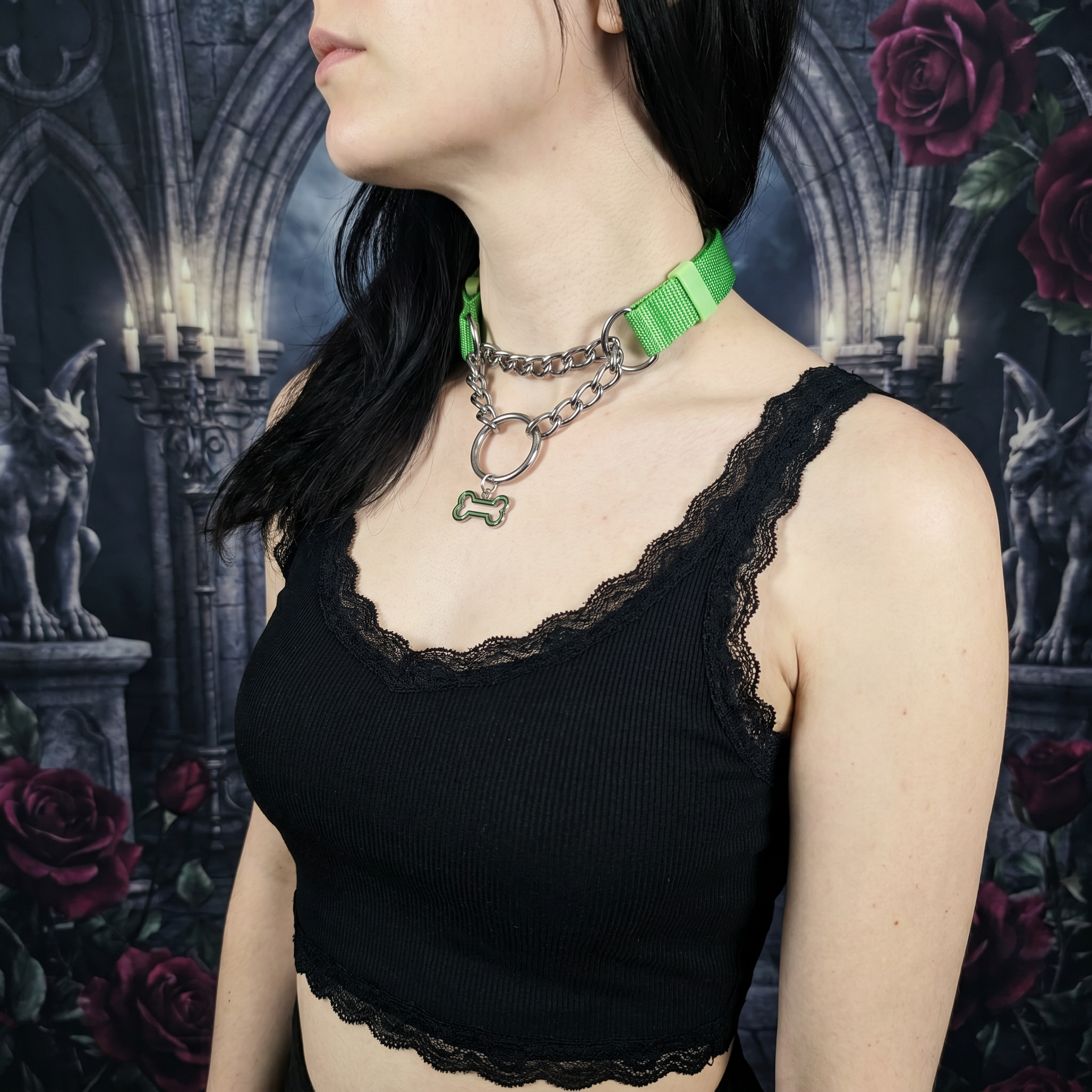 Person wearing a black lace top with a green collar against a dark, gothic-style background with roses and statues.