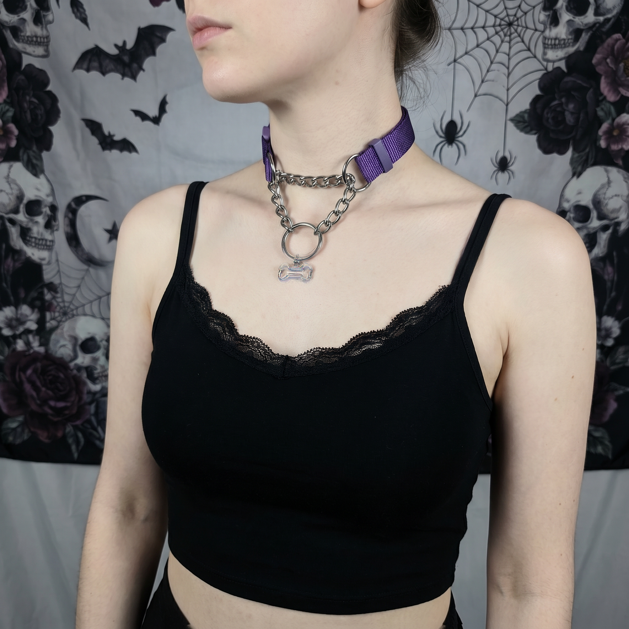 Person wearing a black lace top with a purple choker against a dark, decorative background.