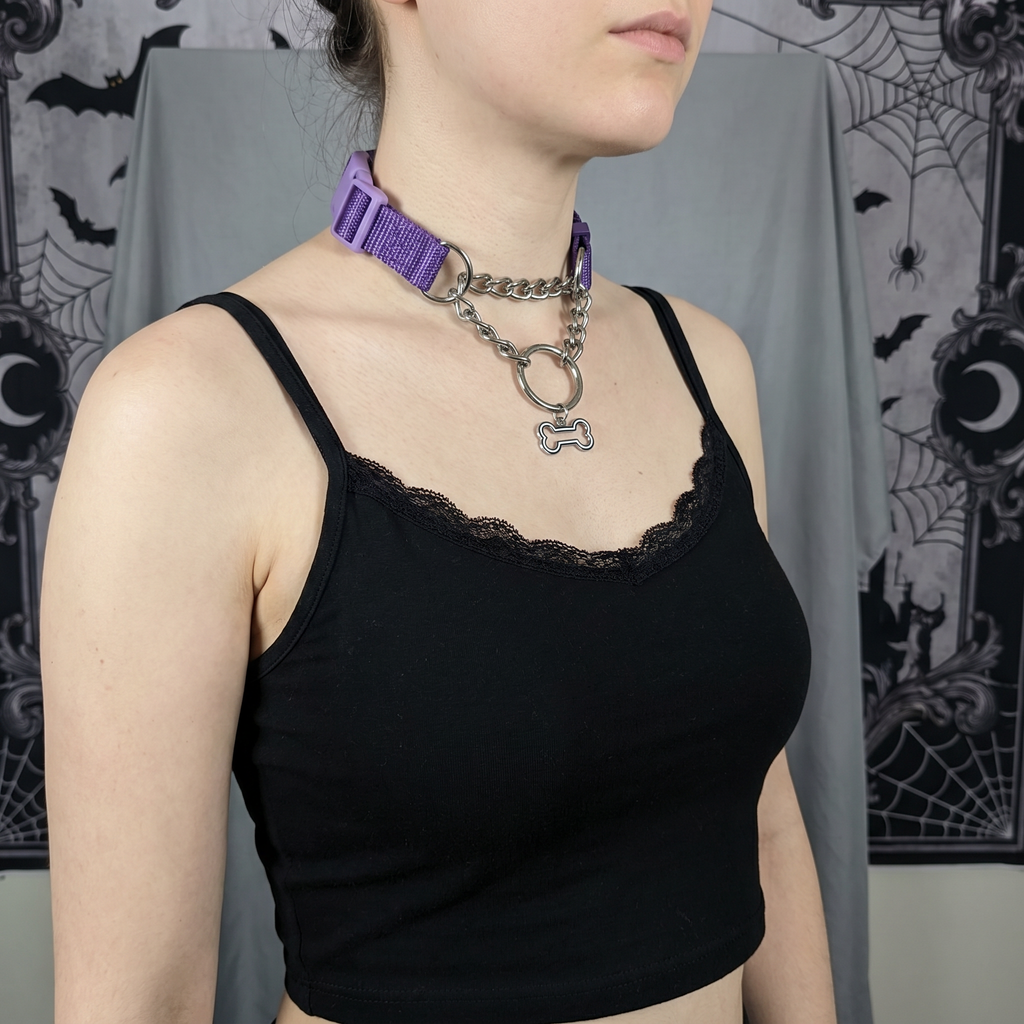 Person wearing a black tank top and purple dog collar with chain, against a decorative backdrop.